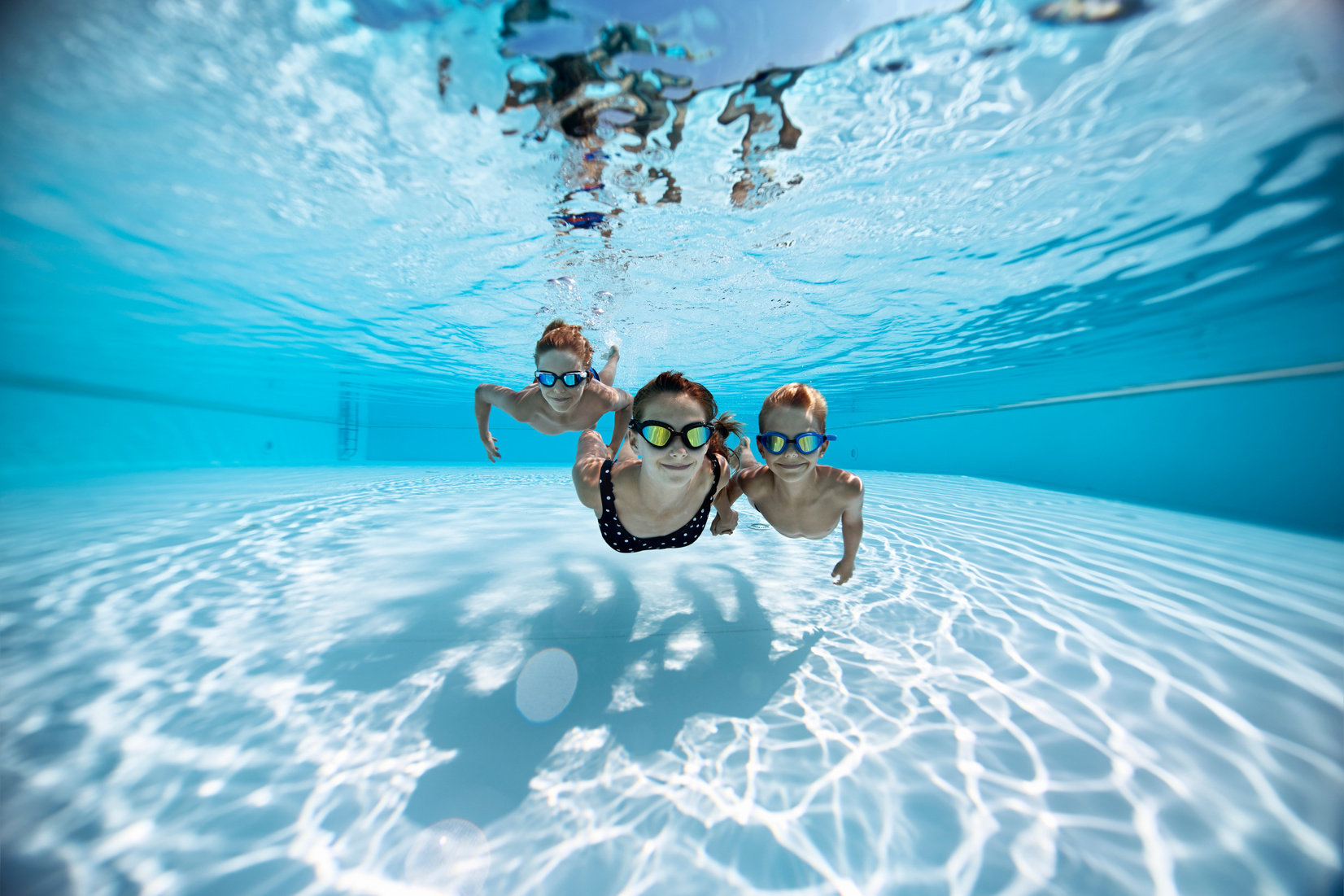 Three happy kids swimming underwater in pool